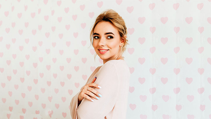 young woman hugging her self in front of a background of pink hearts