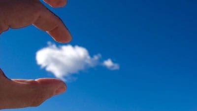 fingers holding a cloud in a blue sky