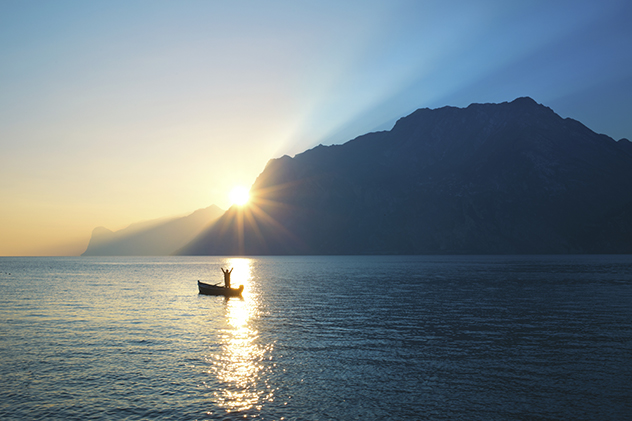 woman cheering in a boat while the sun comes over the mountain