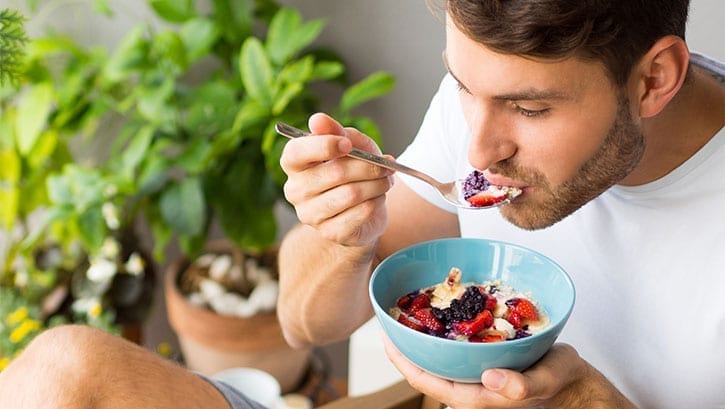 White man eating cereal with berries outdoors