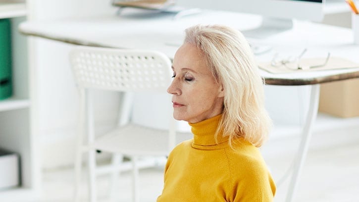 older woman meditating in her home office