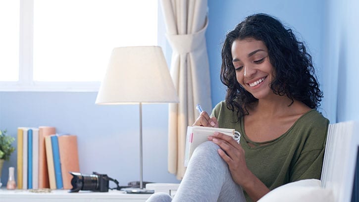 young woman writing in her journal on her bed