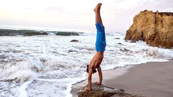 man doing a handstand by the ocean