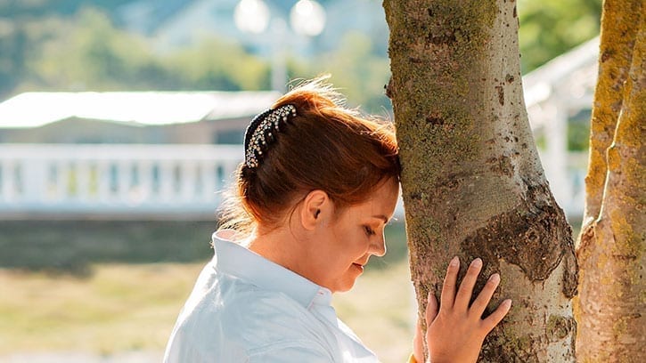 woman leaning her head against a tree trunk