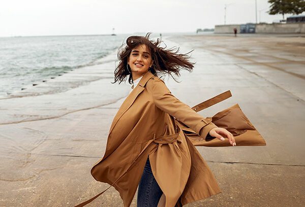 woman twirling at the beach in a trench coat