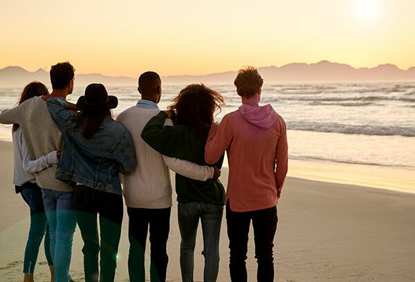 Group of young adults watching the sunrise on a beach in winter.