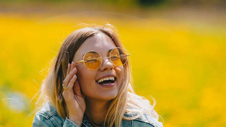 young woman laughing in a field with yellow sunglasses