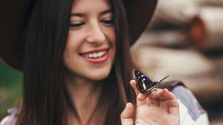 young woman in a hat holding a black butterfly on her fingers