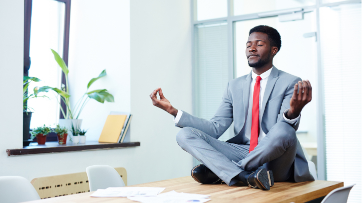 Elegant businessman in red tie and grey suit sitting in pose of lotus on desk