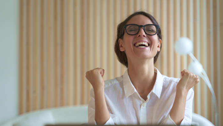 Excited latina woman freelancer clenched her fists with joy and delight with head raised up as if shouting hurray, celebrates joy of finished difficult business project. Remote work concept