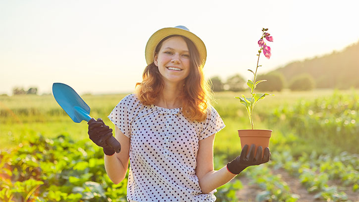 teenage girl in field holding a plant and trowel