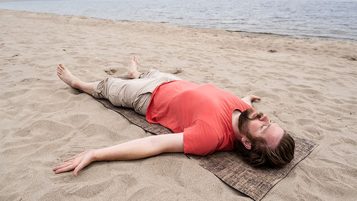 Bearded man does yoga, he does Savasana exercise, relaxes in Corpse posture lying on rug