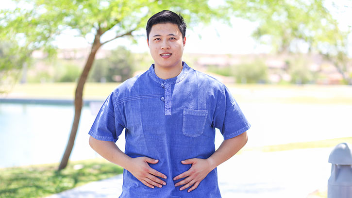 young Asian man with blue shirt in park with hands on abdomen