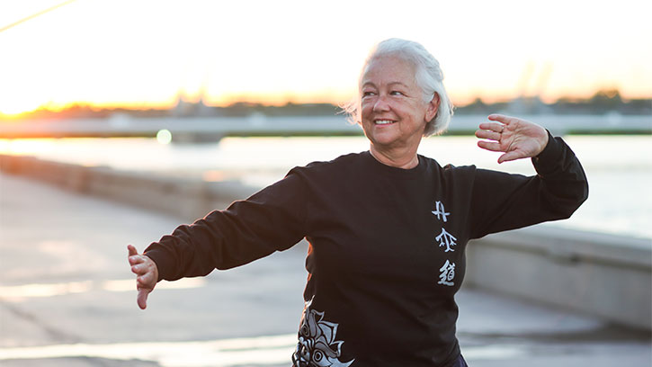 older woman in black shirt in park doing tai chi posture