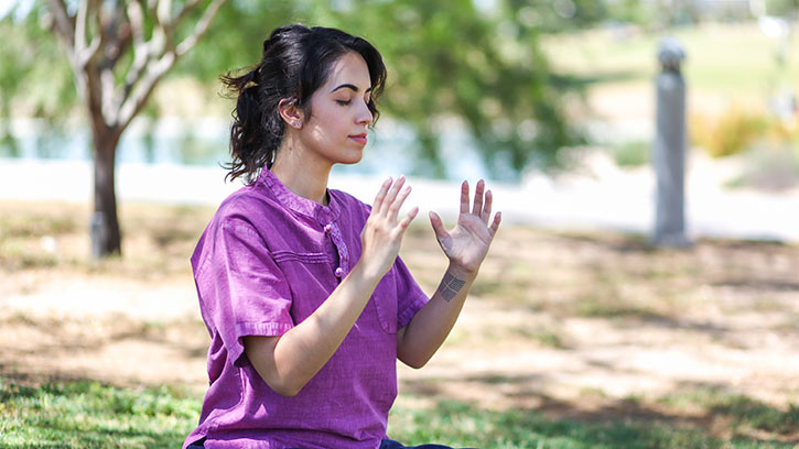 woman in purple shirt in a park with hands facing each other in front of her chest