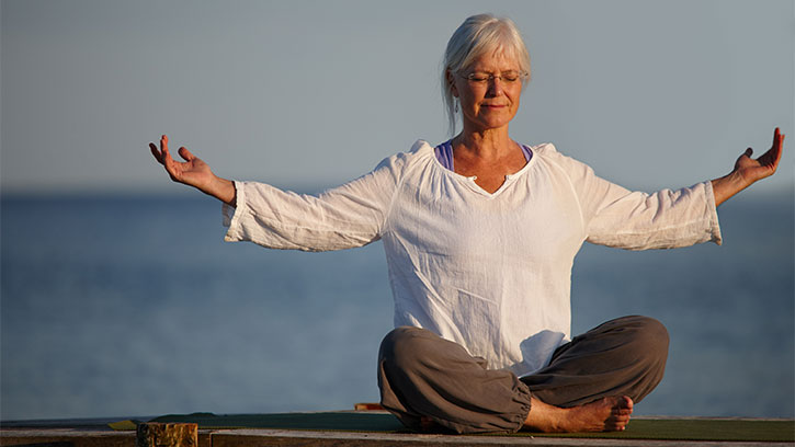 older woman sitting on an ocean pier meditating