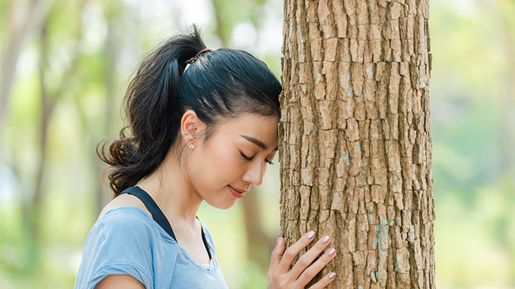 young woman rests her forehead on a tree trunk
