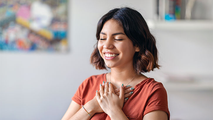 Thankful Arab Woman With Both Palms On Chest Standing Indoors