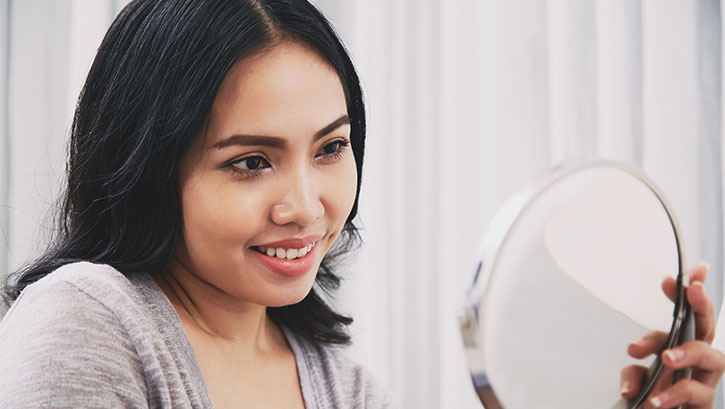 Filipino woman looking at mirror and smiling