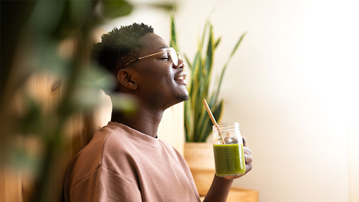 Young man enjoying a green smoothie among green indoor plants