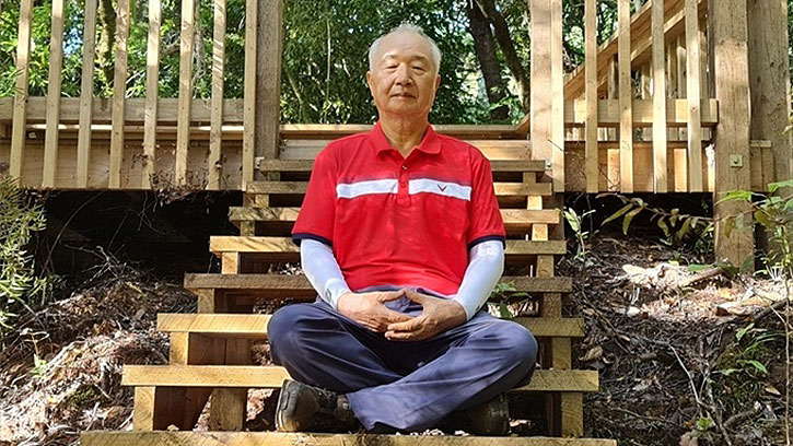 Ilchi Lee sitting on wooden steps in a New Zealand forest