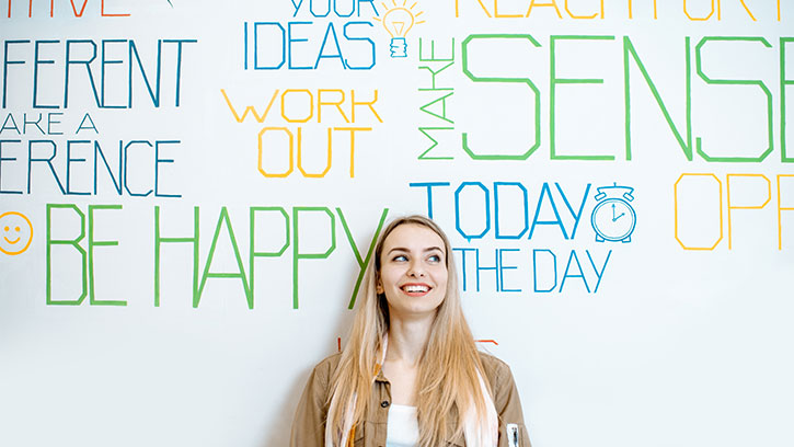 happy young woman leaning against a white wall with positive affirmations