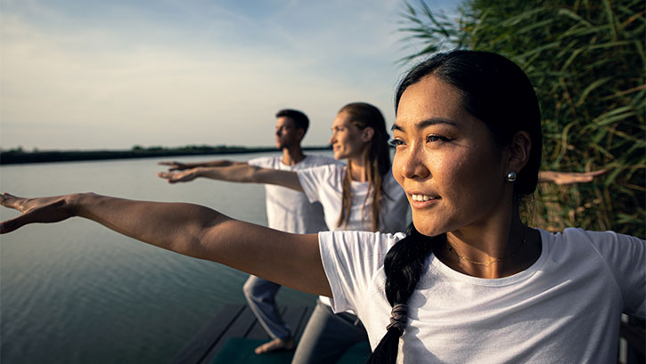2 women and a man doing tai chi by a lake
