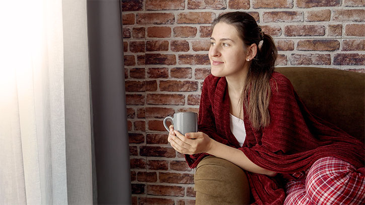 woman on couch looking out the window holding a mug
