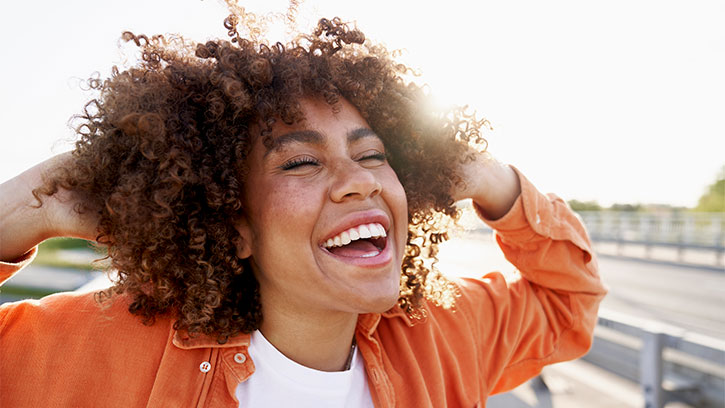 Ilchi Lee Blog Post Thumbnail: woman laughing in the sunlight with her hands in her hair