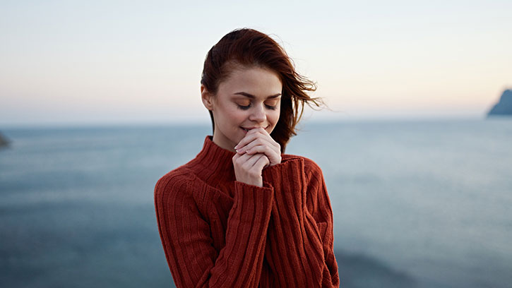 Woman enjoying ocean view at sunrise in sweater