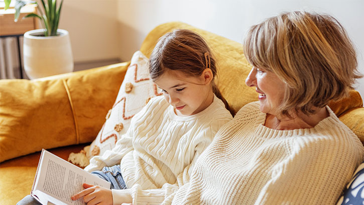 A middle-aged lady smiles at a little girl and holds a book. 