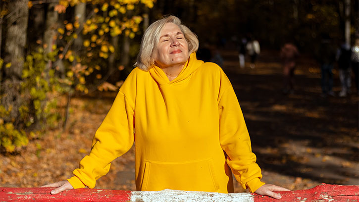 woman in yellow hoodie taking a deep breath near trees while leaning on the railing