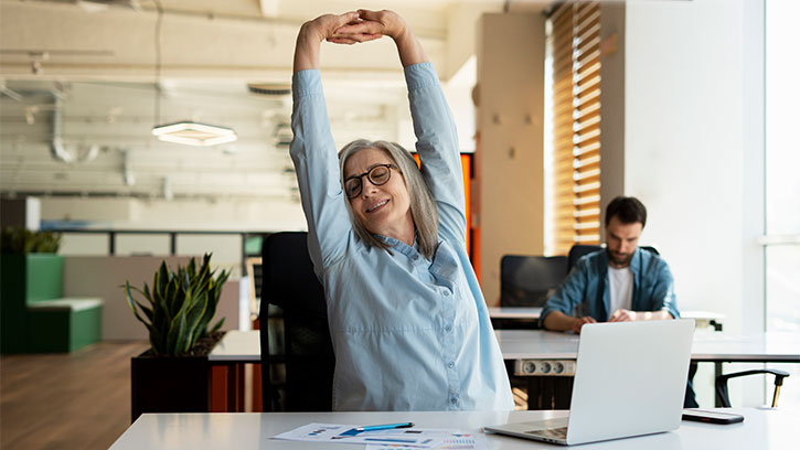 Woman Stretching at Desk in Modern Office